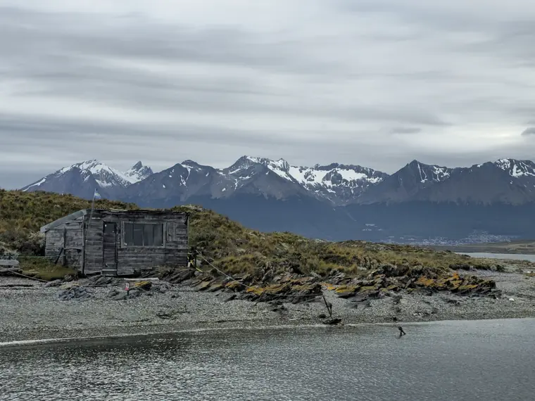 Wooden hut on a shore below snowy mountains